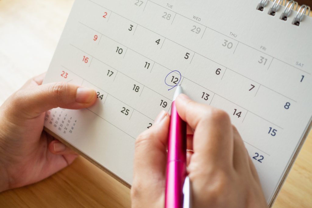 A close-up of a person circling the date 12th on a calendar with a pink pen.