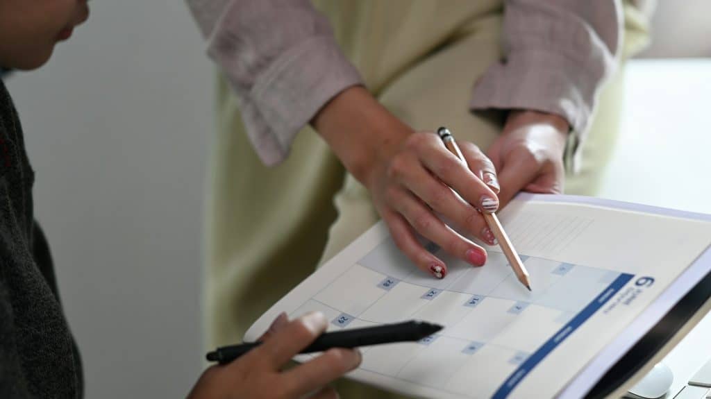 Close-up of two people discussing and pointing at a calendar in a planner, with one person holding a pencil.