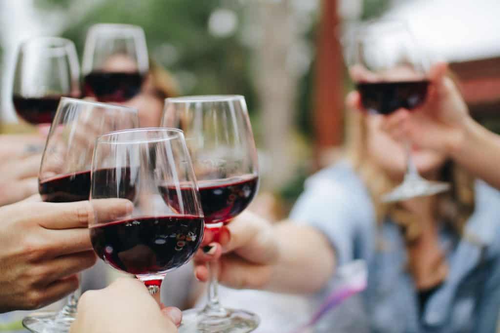 A group of people raising their glasses of red wine in a toast, with some faces blurred in the background, creating a celebratory and joyful atmosphere.