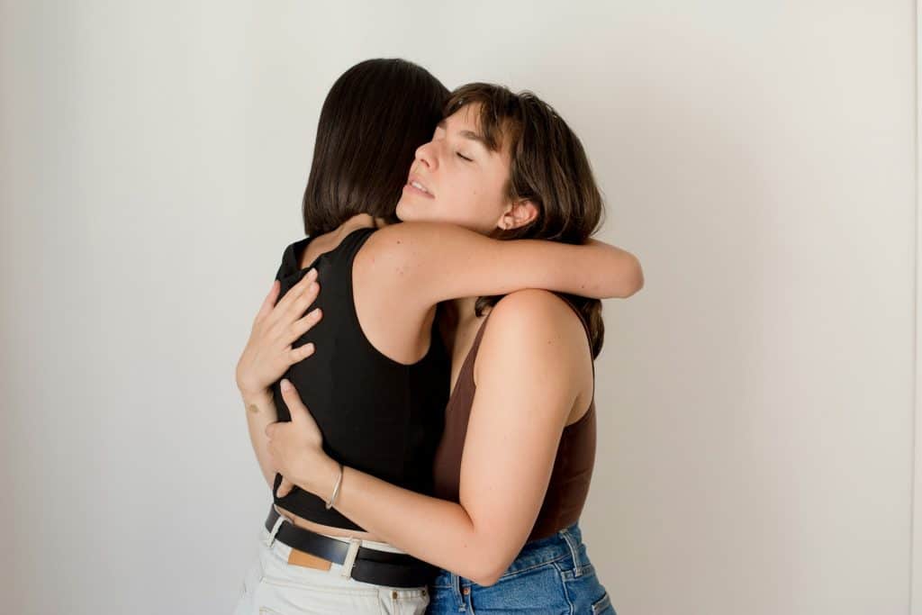 Two women hugging each other, one with short hair and the other with shoulder-length hair, both with expressions of comfort and relief.